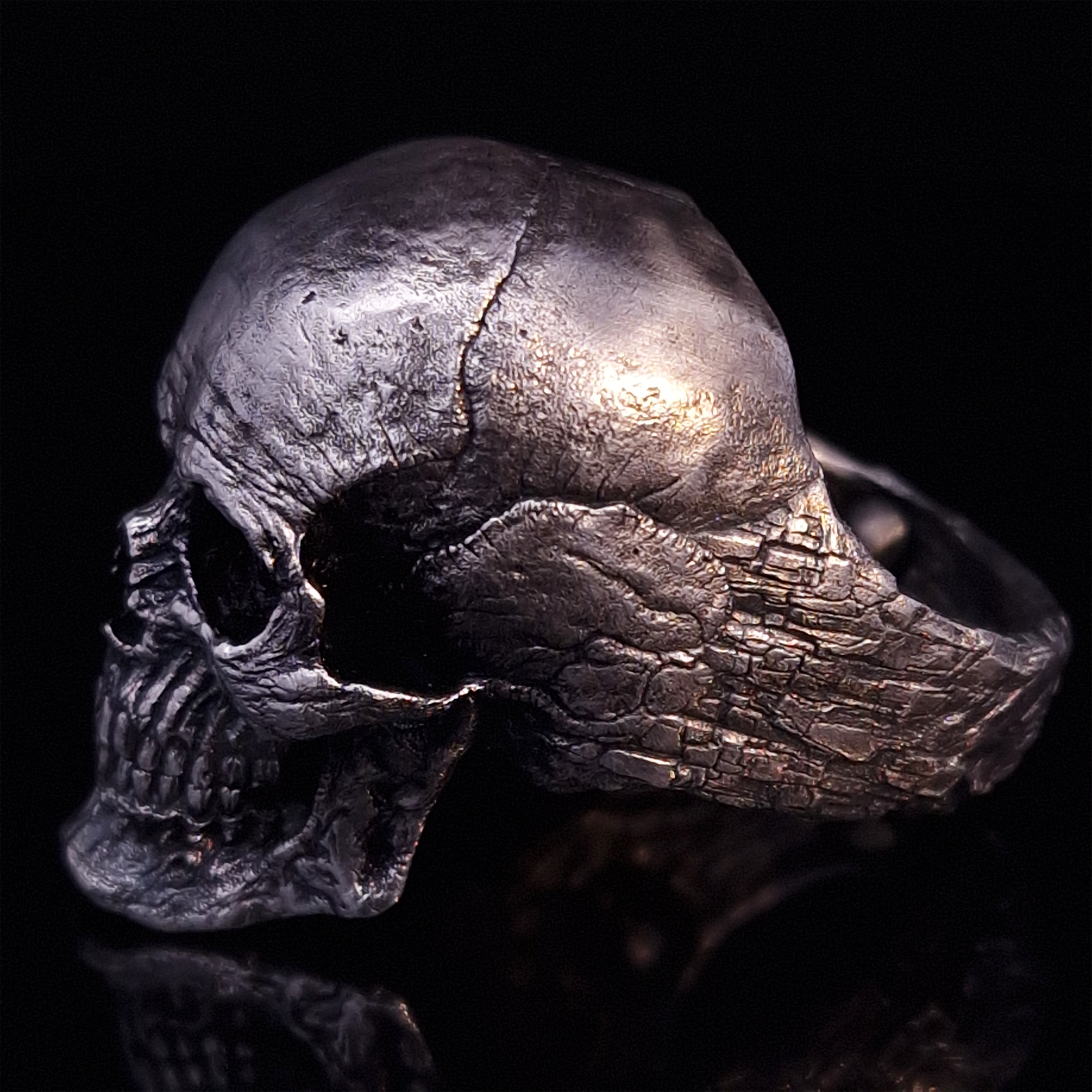Side-left view highlighting the detailed band of the Invidia Mortis ring in the Fallen finish, shown on a turntable with a black background.