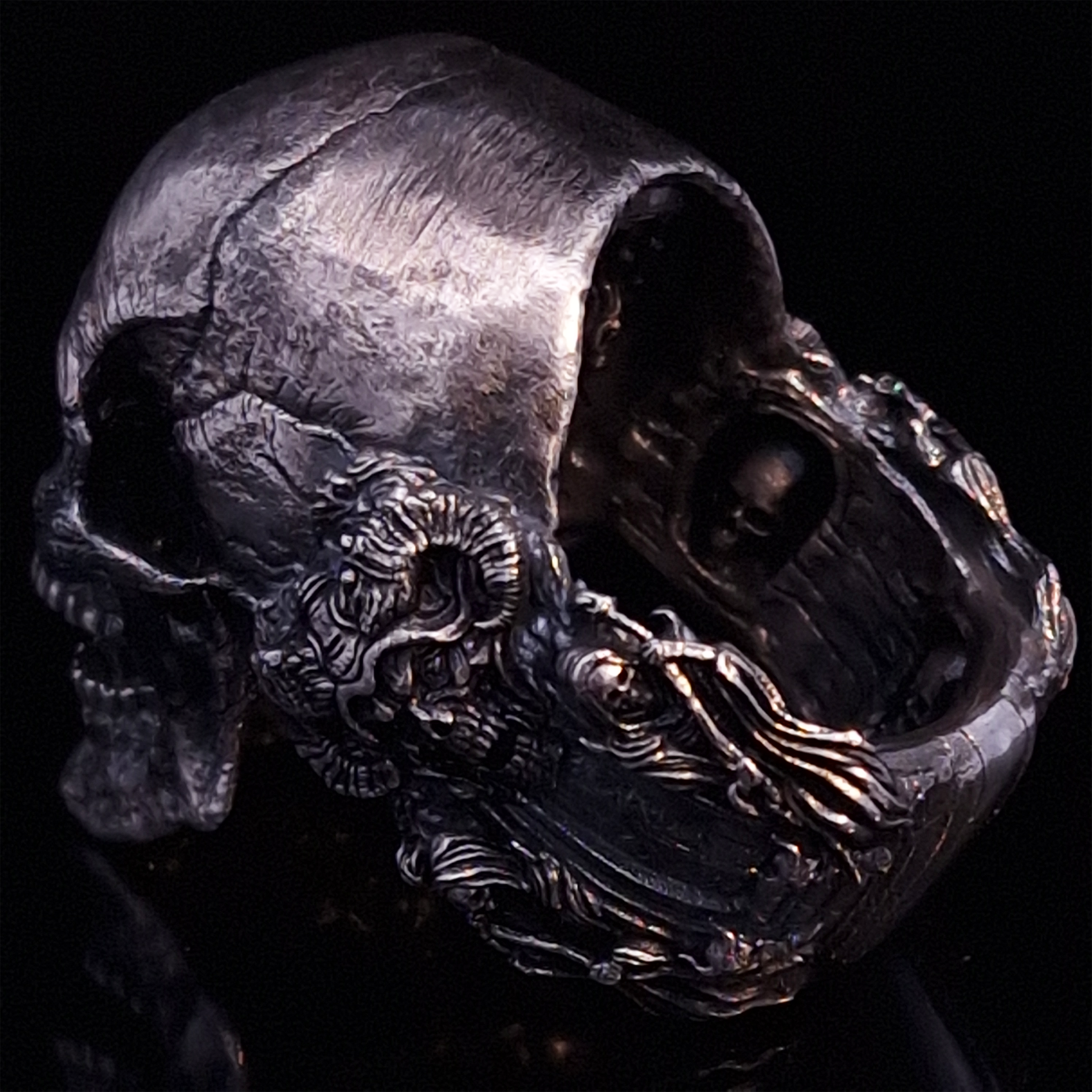 Back-left view of the Nexus Mortis ring in the Fallen finish, focusing on the reaper band, on a turntable with a black background.