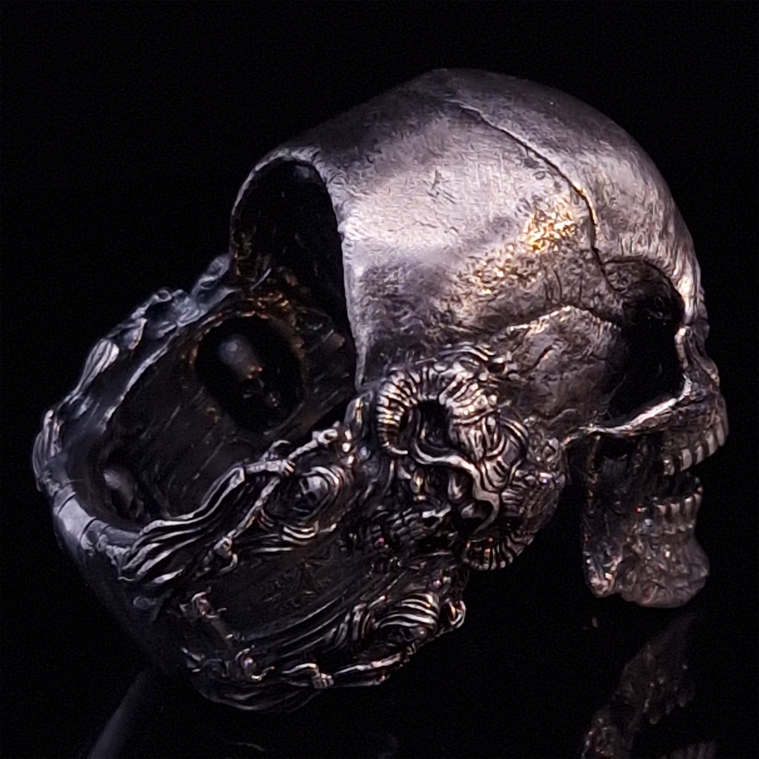 Back-right view of the Nexus Mortis ring in the Fallen finish, focusing on the reaper band, on a turntable with a black background.