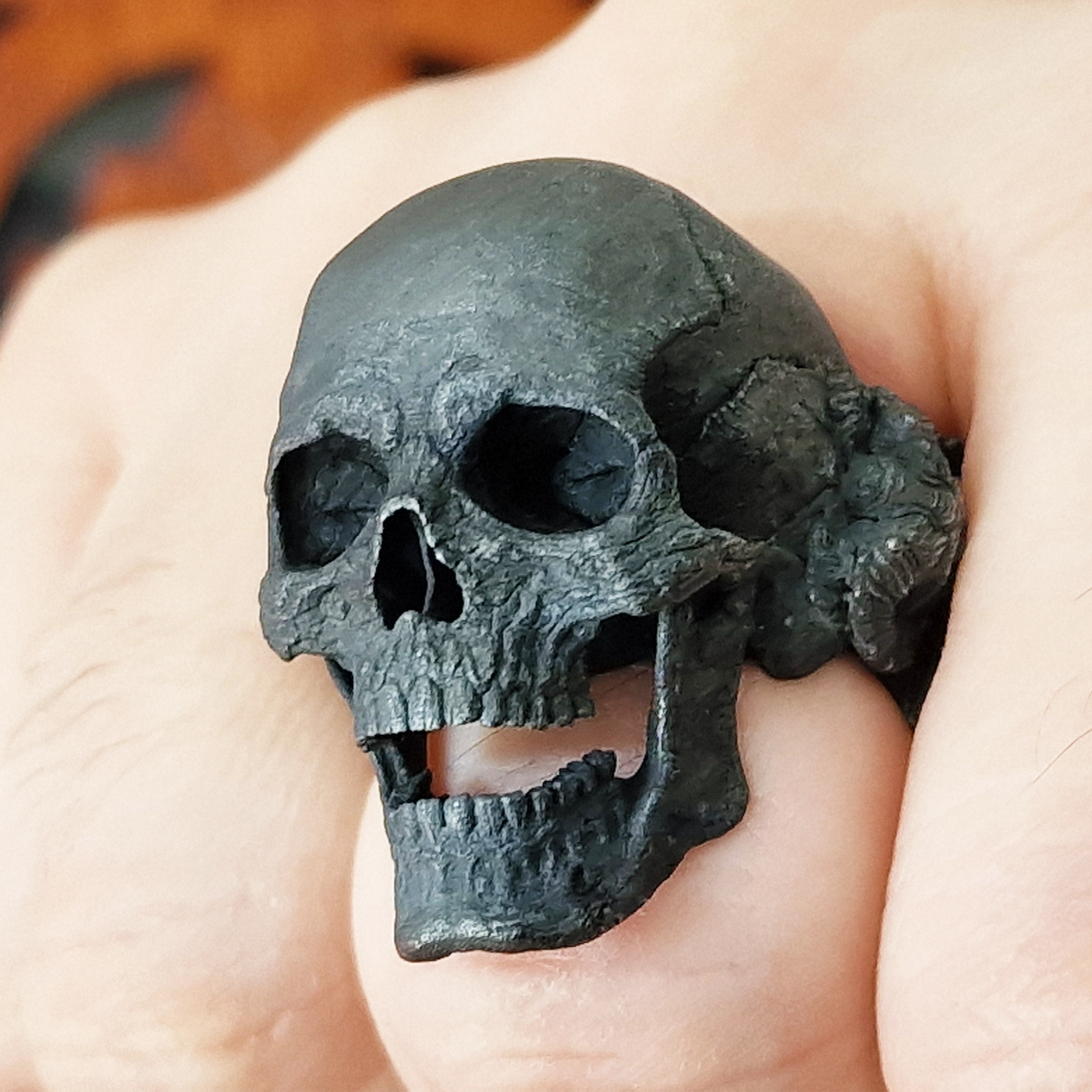 Fist pointed toward the camera in natural light, wearing the Nexus Mortis ring in the Revenant 3 finish, highlighting its details and texture.