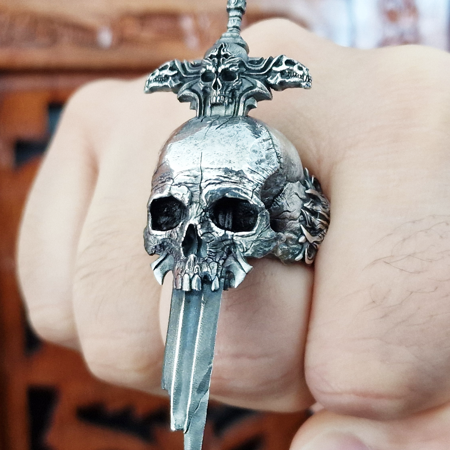 Fist pointed toward the camera in natural light, wearing the Adversarius Mortis ring in the Fallen finish, highlighting its details and texture.