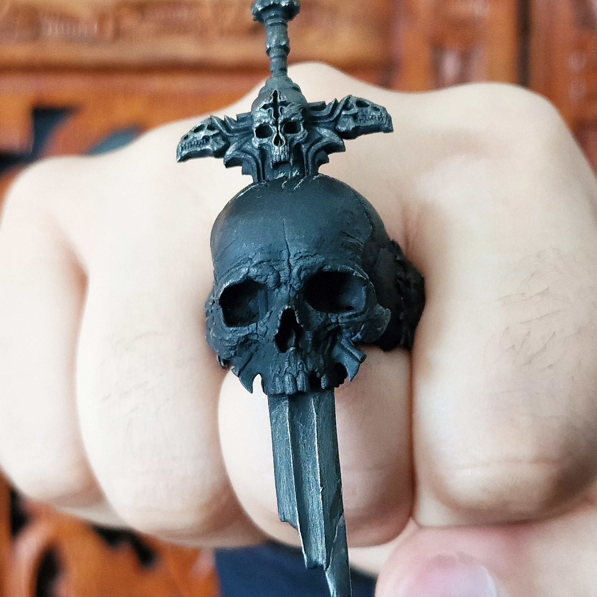 Fist pointed toward the camera in natural light, wearing the Adversarius Mortis ring in the Revenant 2 finish, emphasizing the matte black details.