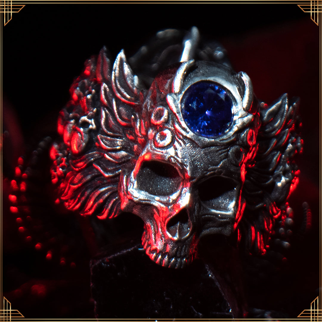 Close-up of the Sword of Damocles ring in the Fallen finish, highlighting the detailed skull design and gemstone on the back of the band, resting on a black obsidian rock.